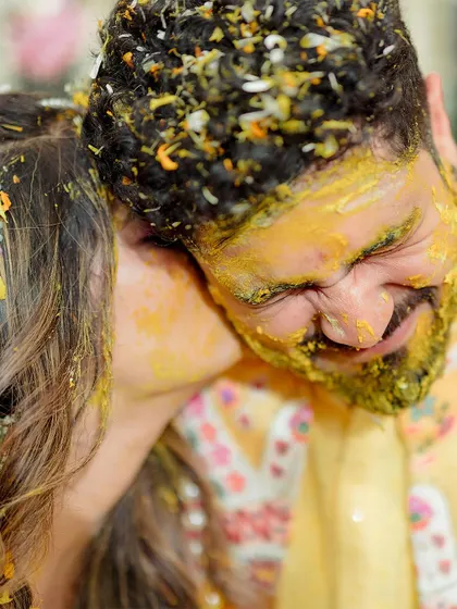 A sweet and playful kiss on the cheek, a candid moment of affection during the messy and fun Haldi celebration.