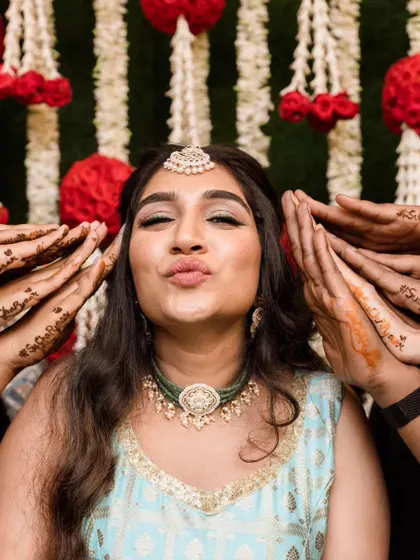Fun and candid moments from a mehendi ceremony. The bride's makeup is fresh and playful, with a winged liner and glowing skin, perfect for celebrating with her loved ones. The hairstyle is a soft half-updo with pretty accessories.