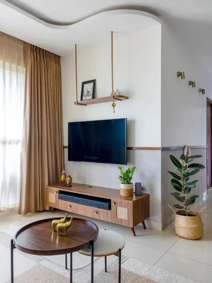 A classic living room with a rustic wicker TV unit, textured walls, and a curved false ceiling detail.