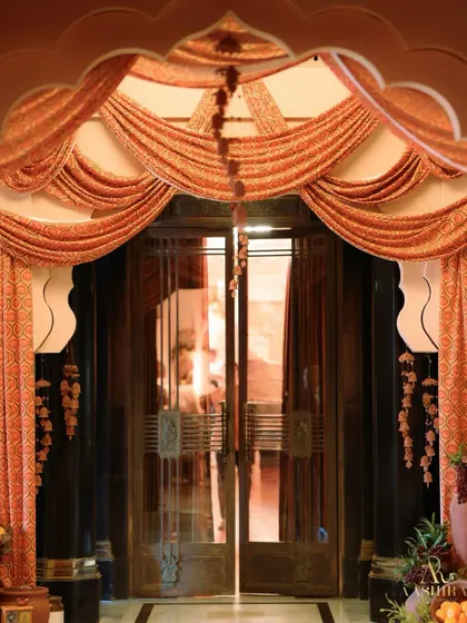 An ornate doorway draped with beautiful printed fabric, with hanging floral tassels and large pots of fruit and flowers on either side.