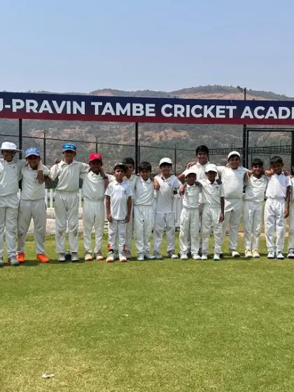 A junior team stands proudly on the field for a photo, with the practice nets and our academy banner visible behind them.