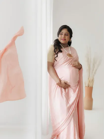 This portrait captures a gentle, happy expression. The soft makeup and flowing saree create a dreamy, romantic vibe for this maternity shoot.
