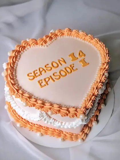 A heart-shaped vintage cake with the message "Season 14, Episode 1," a creative way to celebrate a 14th anniversary.