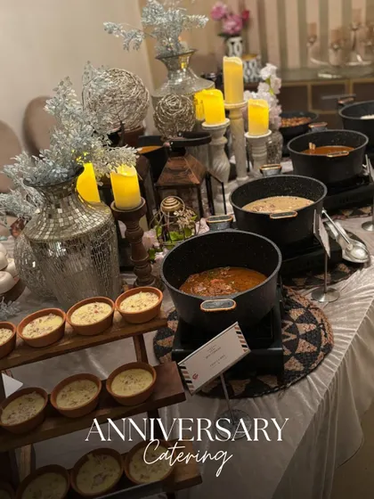 An elegant anniversary catering setup with a silver and white theme. The buffet table is beautifully decorated with candles and metallic accents, creating a romantic atmosphere.