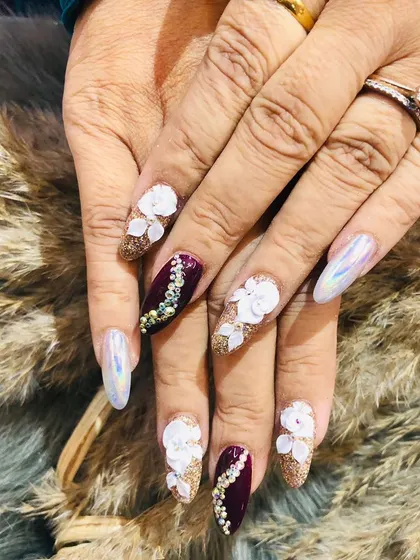 A truly glamorous festive set. These nails feature a mix of glitter, chrome, 3D floral designs, and intricate stone work in a rich maroon and gold palette.
