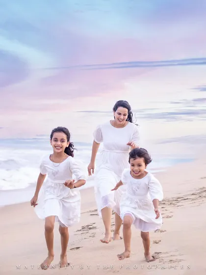 A mother and her two daughters share a joyful run along the shoreline. Dressed in simple white, their connection shines against the pastel colors of the sky, creating a timeless memory of motherhood and sisterhood.