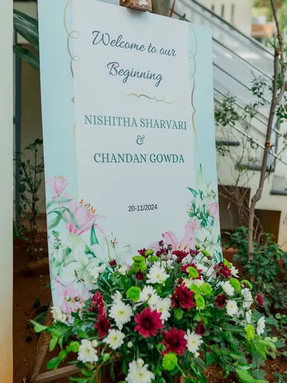 A simple and elegant welcome sign for an intimate engagement, placed in a garden setting and adorned with a fresh bouquet.