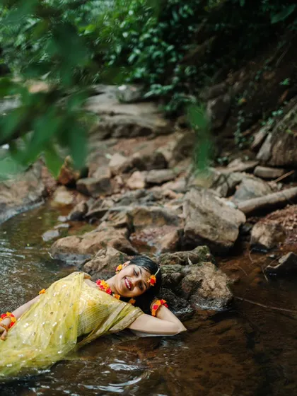 A stunning and unique Haldi portrait of a bride lying peacefully in a gentle stream, surrounded by nature.