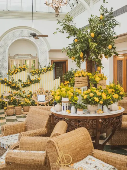 A wide shot of the lemon and sunflower themed Haldi decor, showing the central seating area, wicker chairs for guests, and the overall cheerful ambiance.