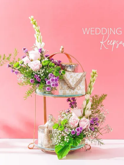 I love creating these multi-level keepsake displays. This two-tiered stand holds various small gifts and wedding keepsakes, all adorned with fresh flowers. It’s a beautiful way to present a collection of thoughtful items.