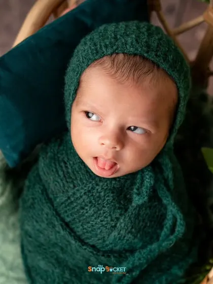 A moment of curiosity! This baby, still cozy in his green wrap, peeks out with a funny expression. It shows that we can capture both sleepy and awake moments.