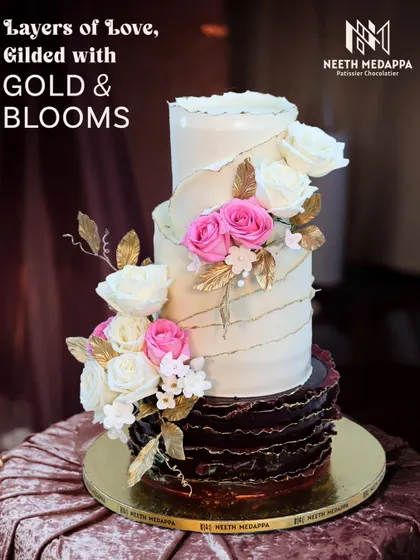 Layers of love, gilded with gold and blooms. This dramatic wedding cake combines a dark chocolate ruffle tier with white tiers adorned with sugar flowers and golden leaves.