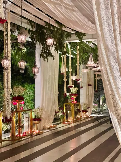 An elegant indoor-outdoor transition, with striped flooring, sheer white drapes, and hanging floral arrangements in a red and white palette.