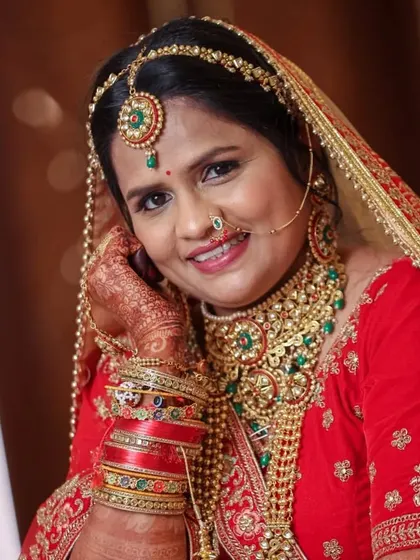 A stunning bride in a classic red lehenga, complemented by my heavy bridal set in green and red Kundan. The layered necklaces create a truly majestic look.