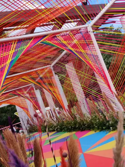 A dynamic and colorful entrance tunnel made of intersecting rainbow-colored strings, creating a vibrant and artistic passageway for a carnival-themed event.