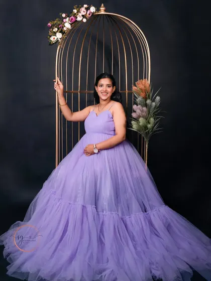 A regal portrait of the mom-to-be seated in the golden birdcage. The lavender gown and floral decorations create a majestic and beautiful image.