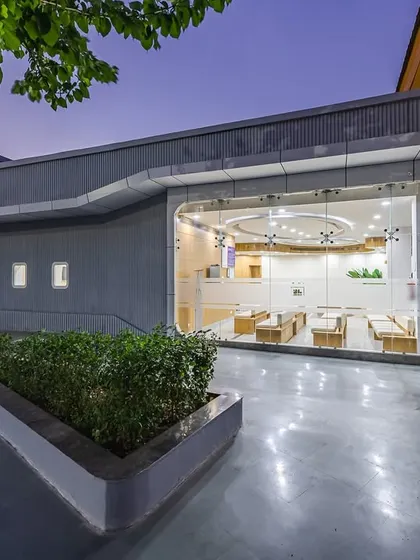 As dusk settles, the illuminated interior of the Northern Railway Diagnostic Centre creates a reassuring presence. The warm lighting highlights the clean, modern design and signals a place of care and technological advancement, even after dark.