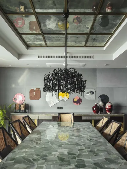 A full view of the dining room, where the light green aventurine tabletop reflects the dramatic chandelier and the art on the walls. The mirrored ceiling adds another layer of glamour and depth to the space.