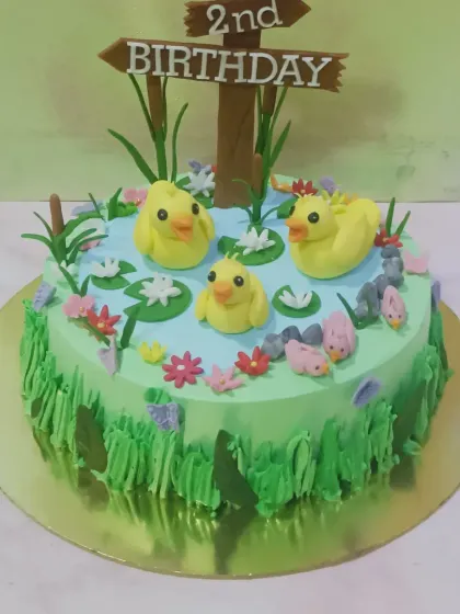 A charming duck pond cake for a 2nd birthday. This cake features little yellow fondant ducks swimming in a blue "pond" surrounded by green buttercream "grass."