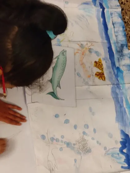 A child works on a large mural depicting the story of life on Earth, drawing different prehistoric sea creatures.
