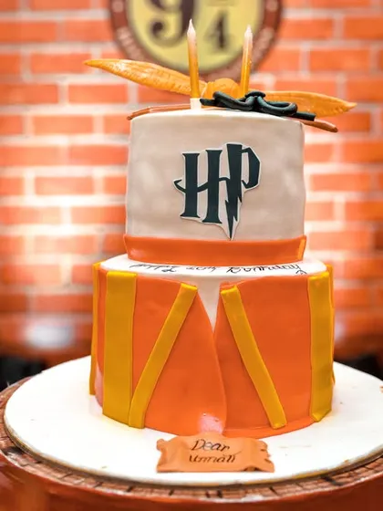 A magical Harry Potter themed cake. This two-tiered creation is designed to look like a drum from the Hogwarts marching band, complete with the HP logo and a golden snitch on top.
