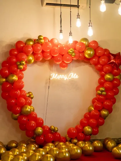 Our heart-shaped balloon arch is a popular choice for proposals. Made with vibrant red and gold balloons, it frames the moment perfectly and includes a 'Marry Me' neon sign at its center.