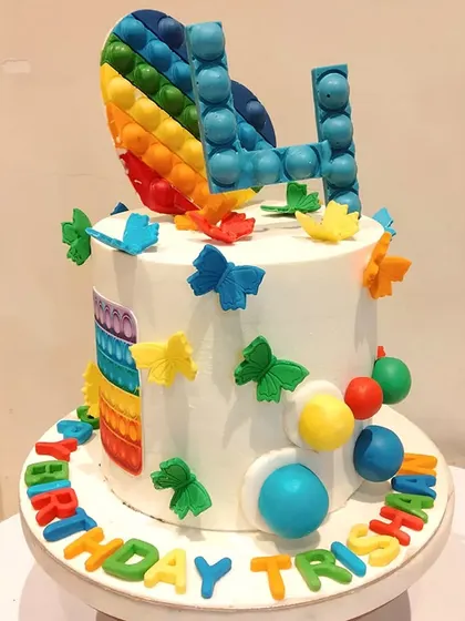 A trendy and colourful pop-it themed cake. This design incorporates the popular fidget toy into the cake itself, with edible bubbles and a rainbow heart topper.