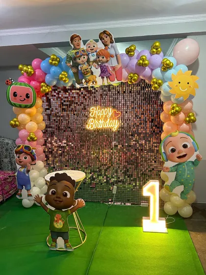 A Cocomelon first birthday setup featuring a pink shimmer wall, a neon sign, and cutouts of all the favorite characters.