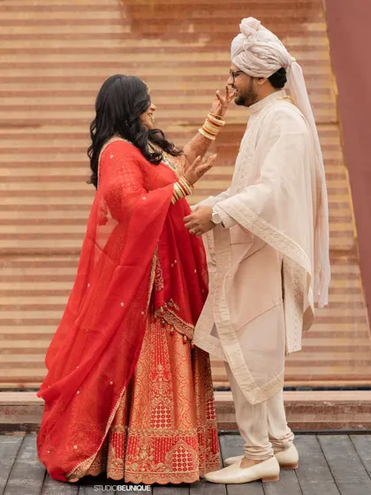 A fun, candid interaction between the bride and groom, their vibrant red and classic ivory outfits creating a beautiful contrast.
