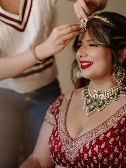 The getting ready process is so special. Here, I'm putting the finishing touches on her matha patti, completing her classic red bridal look with a bold lip.