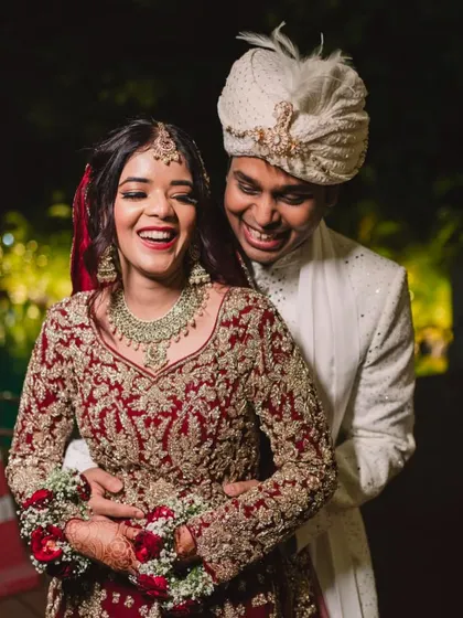 A joyful candid shot of the bride and groom. Her radiant makeup and stunning red lehenga with a long trail create a picture-perfect wedding memory.