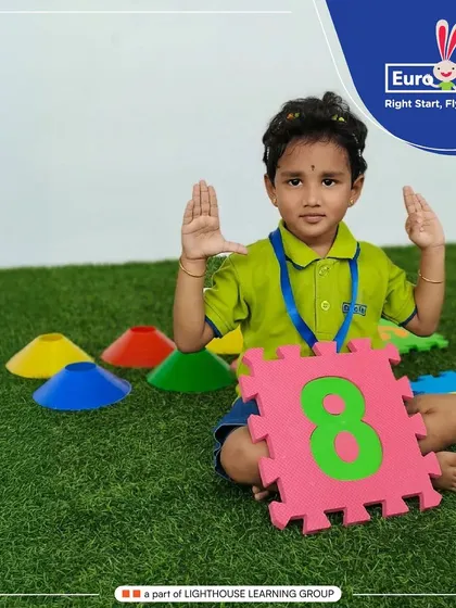 This student holds up eight fingers, matching the number '8' on the large puzzle piece she holds. This multi-sensory activity reinforces number recognition and counting skills effectively.