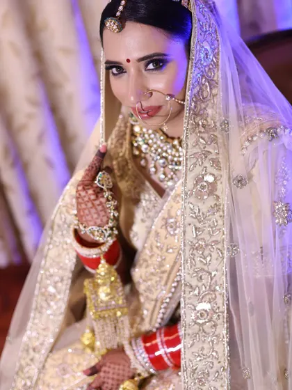 A portrait of a bride in a stunning white and gold lehenga. The veil frames her face beautifully, and her direct gaze is powerful.