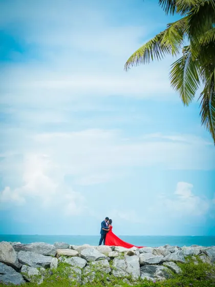 An epic, wide-angle pre-wedding photograph of a couple by the ocean, creating a sense of grandeur and romance.