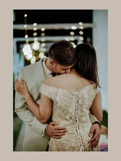 A romantic and intimate shot from behind, with the groom kissing the bride's shoulder, highlighting the beautiful lace-up back of her dress.