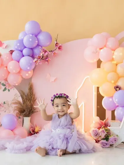 A pastel dream for a first birthday. This beautiful setup with purple, pink, and orange balloons creates a soft and cheerful backdrop for a cake smash session.