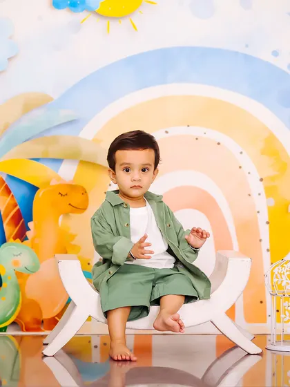 A cool and casual pose from this little boy during his dinosaur-themed photoshoot. The pastel rainbow and friendly dinosaurs create a sweet and modern backdrop.