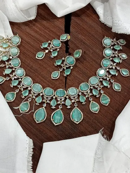 A stunning AD necklace set laid out to show its full design. This piece is available in multiple vibrant colors like ruby red, emerald green, pastel blue, and sapphire blue, featuring teardrop-shaped stones.