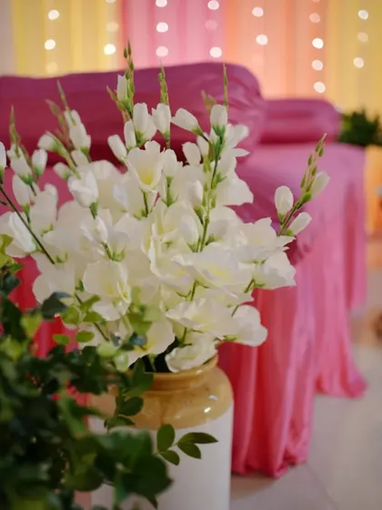A detail shot of a white vase with fresh white flowers, set against a backdrop of pink draping for a Mehendi event. The contrast of colors creates a fresh and modern look.