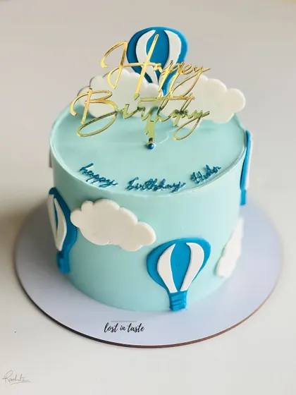 A whimsical hot air balloon themed cake. The light blue buttercream sky, fluffy clouds, and a golden "Happy Birthday" topper make it a delightful choice for a child's celebration.
