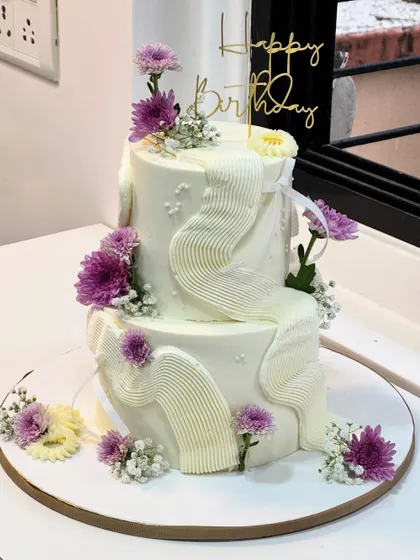 A little birthday magic with soft buttercream waves and fresh purple flowers. This dreamy two-tier cake is a beautiful example of texture and floral artistry combined.