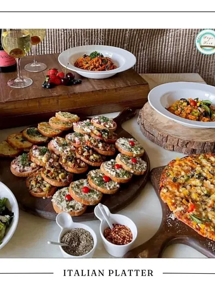 Our Italian Platter, a perfect choice for a festive gathering. It features a beautiful spread of bruschetta, pastas, and pizza, accompanied by a bottle of sparkling wine.