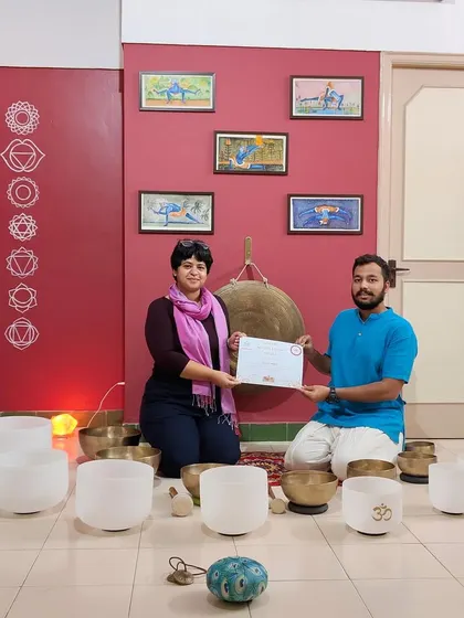 A student receives her Level 1 certification, surrounded by the instruments she has learned to master. This moment signifies her readiness to begin sharing the practice of sound meditation.
