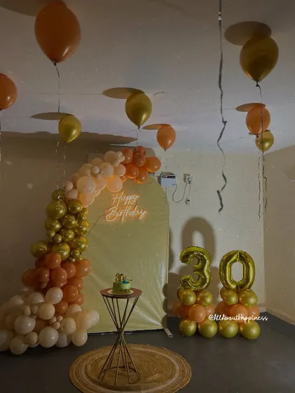 A warm and inviting 30th birthday setup in a common hall. The arch backdrop, neon sign, and earthy-toned balloons create a cozy and celebratory atmosphere.