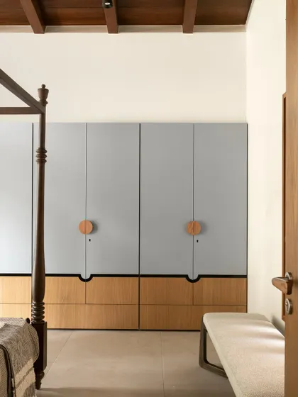 This view showcases the full height of the custom wardrobes and the beautiful contrast between the cool grey, warm wood, and the dark, sculptural bed frame.