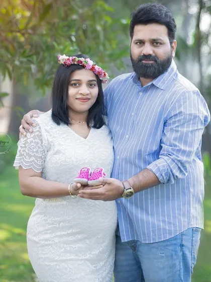 A lovely portrait of parents-to-be holding tiny pink booties. The mother's floral crown and white lace dress add a touch of delicate beauty to this outdoor shot.