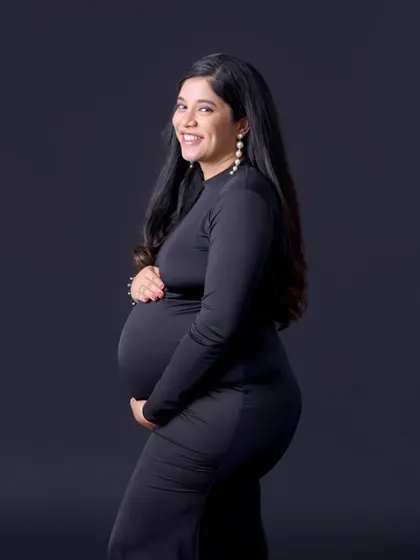 A classic low-key portrait in a simple black dress. The dark background and professional lighting create a sophisticated and timeless image that highlights the baby bump.