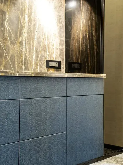 A detail shot of the boardroom bar, highlighting the rich texture of the blue-grained wood cabinetry against the dramatic marble countertop and backsplash. This combination of materials adds depth and a tactile quality to the design.