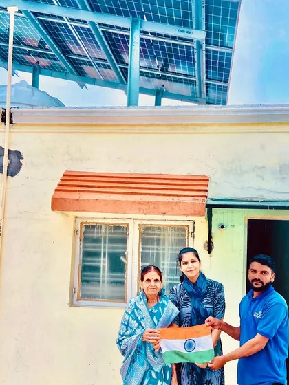 Our team member with two customers outside their home, holding the Indian flag to mark their solar installation.