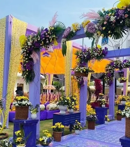 A beautiful Mehendi or Haldi entranceway combining purple and yellow drapes and abundant floral arrangements. This setup creates a welcoming and festive atmosphere for daytime pre-wedding functions.